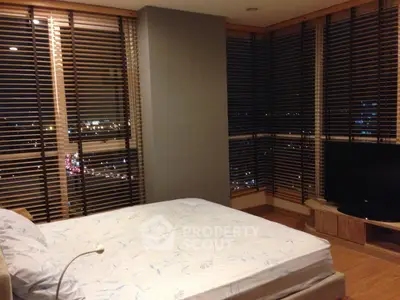 Spacious bedroom with city view and modern blinds in high-rise apartment.