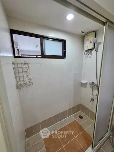 Compact bathroom shower area with tiled walls and floor, featuring a wall-mounted water heater.