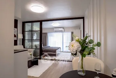 Modern open-plan living room with glass partition leading to a cozy bedroom, featuring elegant decor and natural light.