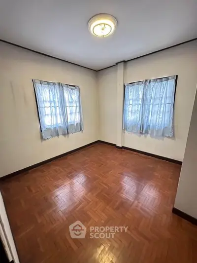 Spacious empty room with wooden flooring and natural light from two windows