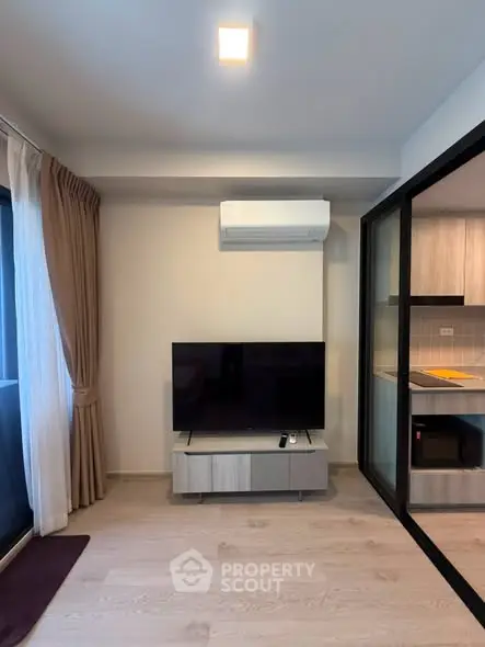 Modern living room with sleek TV setup and adjacent kitchen area in stylish apartment.
