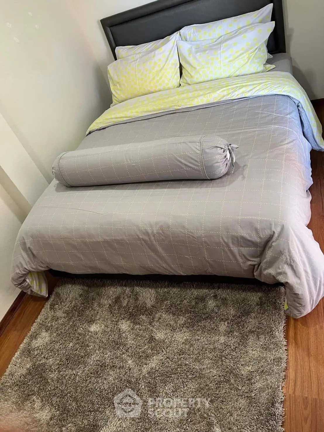 Cozy bedroom with stylish bedding and plush rug on wooden floor, perfect for relaxation.