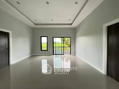 Spacious modern living room with large windows and glossy tiled floors, offering serene views of lush greenery.