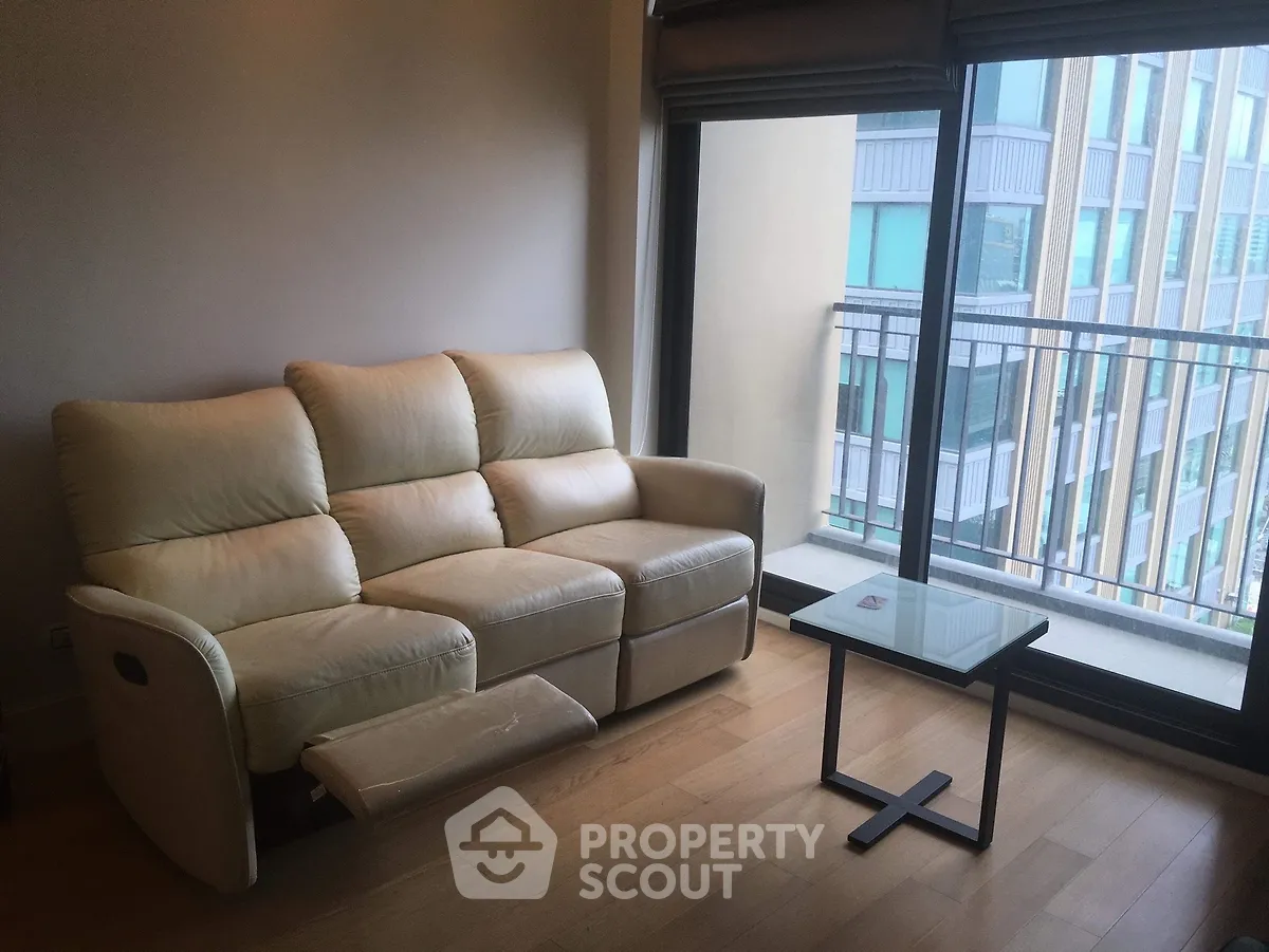 Modern living room with beige sofa and glass table near balcony with city view.