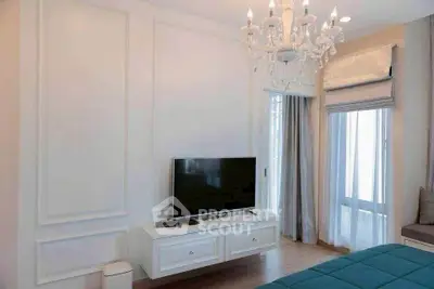 Elegant bedroom with chandelier and TV, featuring stylish decor and natural light.