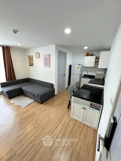 Modern open-plan living room with kitchen, featuring sleek furniture and wooden flooring.