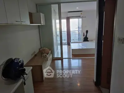 Modern apartment interior with wooden flooring and sliding glass doors leading to a balcony with a view.
