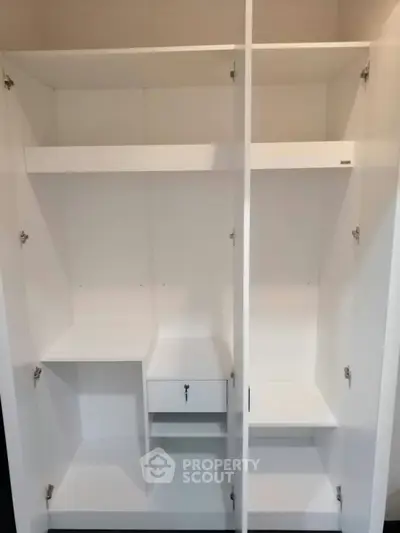 Spacious white built-in wardrobe with shelves and drawer, perfect for organized storage.