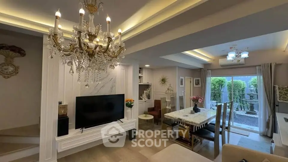 Luxurious living room with elegant chandelier and modern decor, featuring a spacious open layout and garden view.
