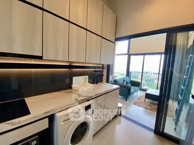 Modern kitchen with sleek cabinets and washing machine, leading to a bright living room with balcony view.