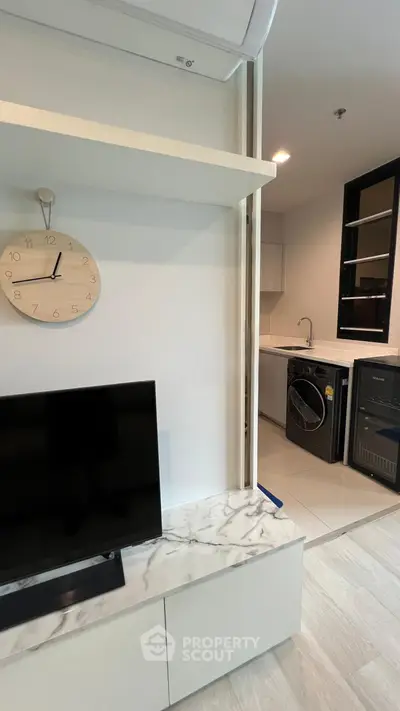 Modern apartment interior with sleek kitchen and stylish living area featuring TV and clock.