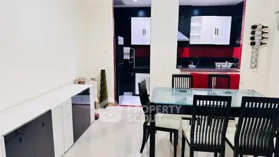 Modern dining area with sleek black and white kitchen, glass table, and stylish chairs.