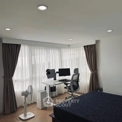 Modern bedroom with study area, featuring a desk, computer setup, and large windows with curtains.
