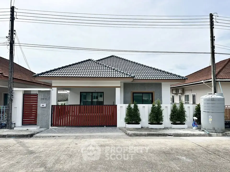 Charming single-story house with tiled roof and red gate, featuring a neat front yard and modern design.