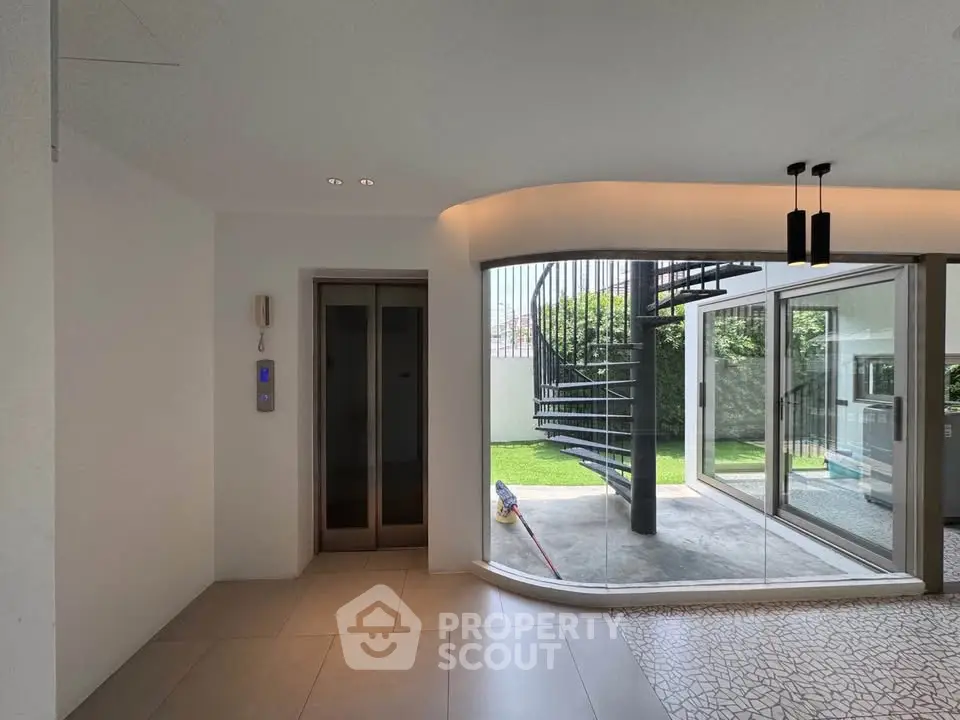 Modern home entrance with elevator and spiral staircase leading to garden view.