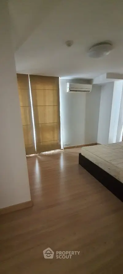 Spacious bedroom with wooden flooring and natural light, featuring an air conditioning unit and modern design.