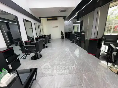 Modern salon interior with sleek black chairs and large mirrors, featuring glossy tiled flooring and stylish decor.