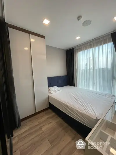 Modern bedroom with large window and sleek wardrobe in a stylish apartment.