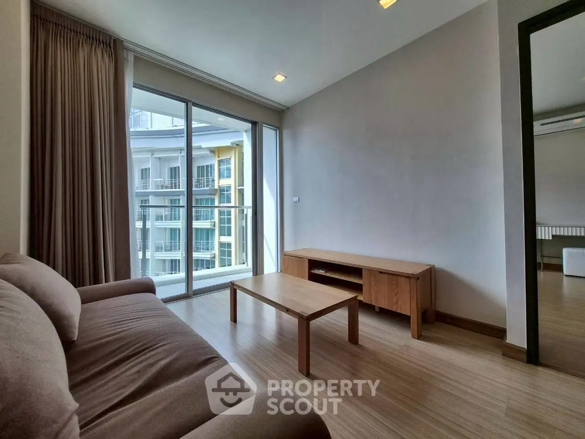 Modern living room with cozy sofa and wooden furniture, featuring large windows and balcony access.