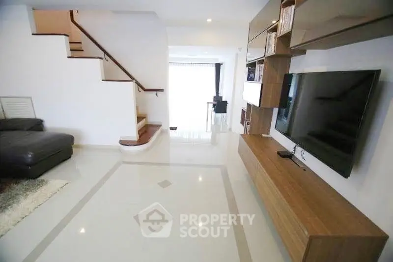 Spacious modern living room with sleek TV setup and elegant staircase.