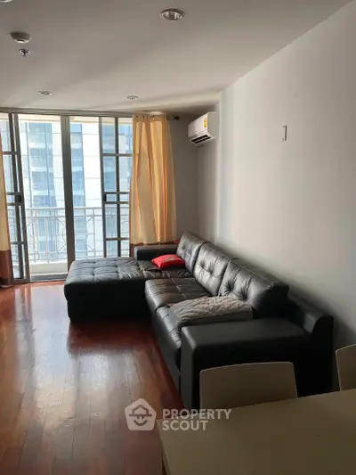 Spacious living room with modern leather sofa and large windows in a high-rise apartment.