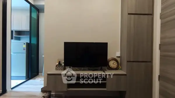 Modern living room with sleek TV stand and view into kitchen with fridge.
