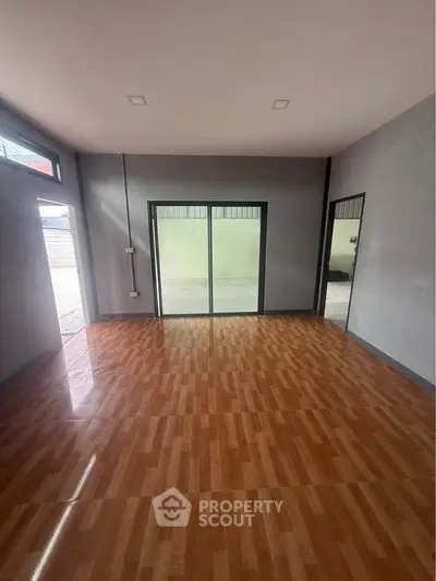 Spacious empty room with wooden flooring and large windows, perfect for customization.