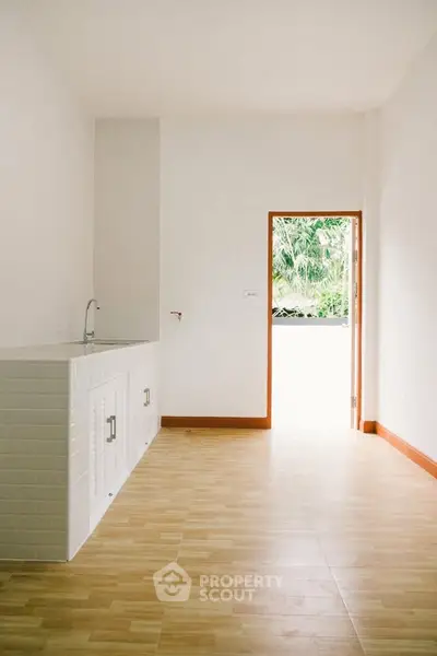 Bright minimalist kitchen with open door leading to lush greenery view.