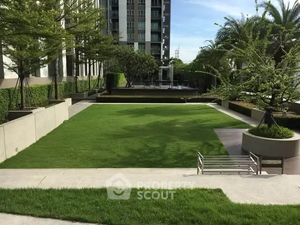 Lush green garden area in modern residential complex with seating and landscaped surroundings.