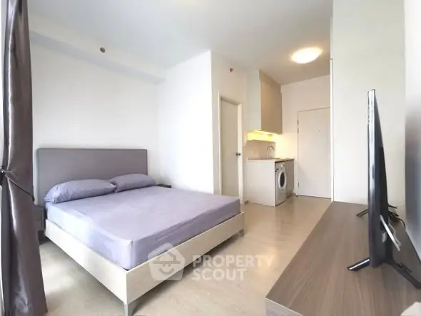 Modern studio apartment with sleek design, featuring a cozy bed and compact kitchen area.