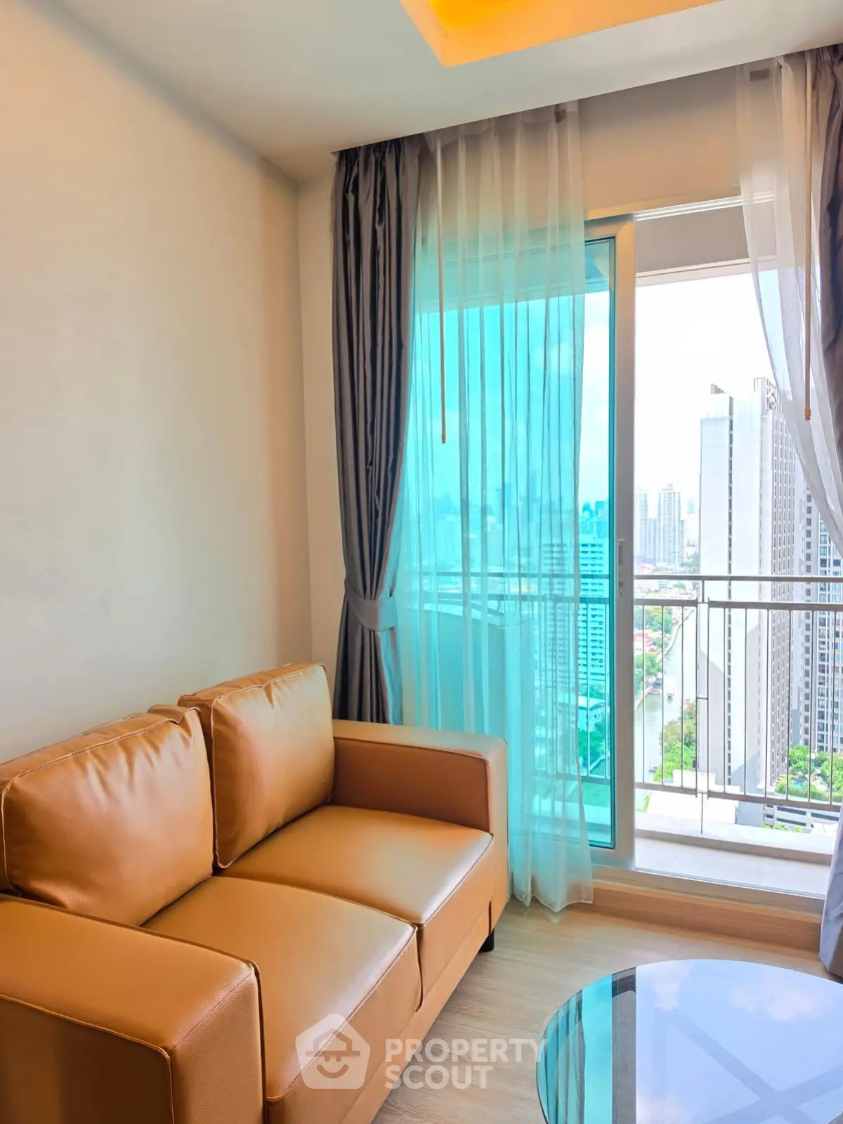 Modern living room with city view from balcony, featuring cozy leather sofa and elegant curtains.