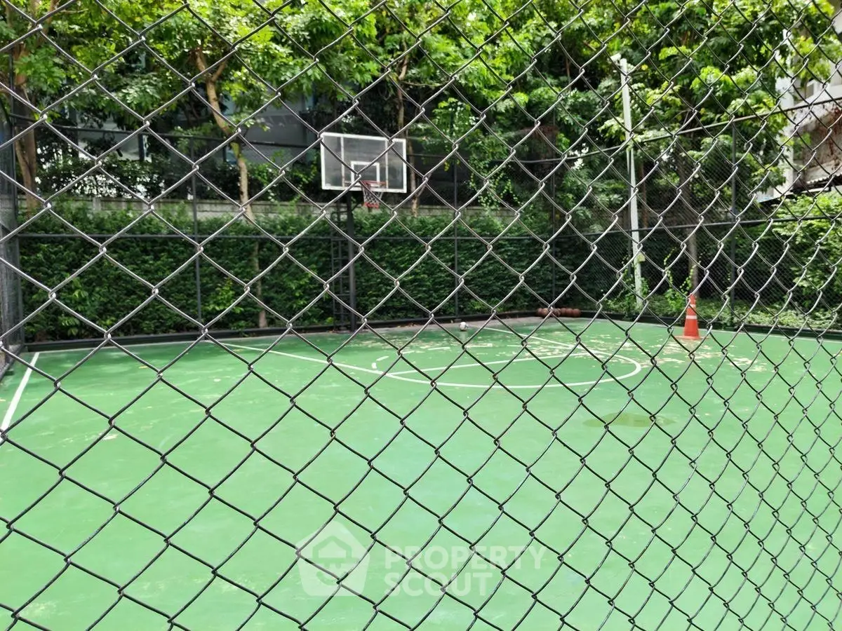 Outdoor basketball court with green surface and surrounding fence in lush garden setting.