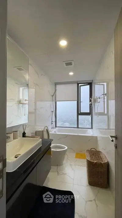 Modern bathroom with large window and sleek fixtures in high-rise apartment.