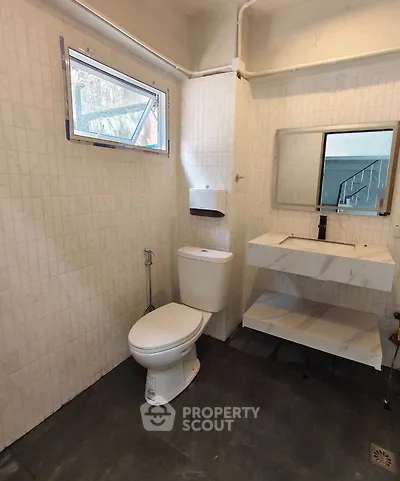 Modern bathroom with sleek fixtures and natural light, featuring a toilet, sink, and wall-mounted mirror.