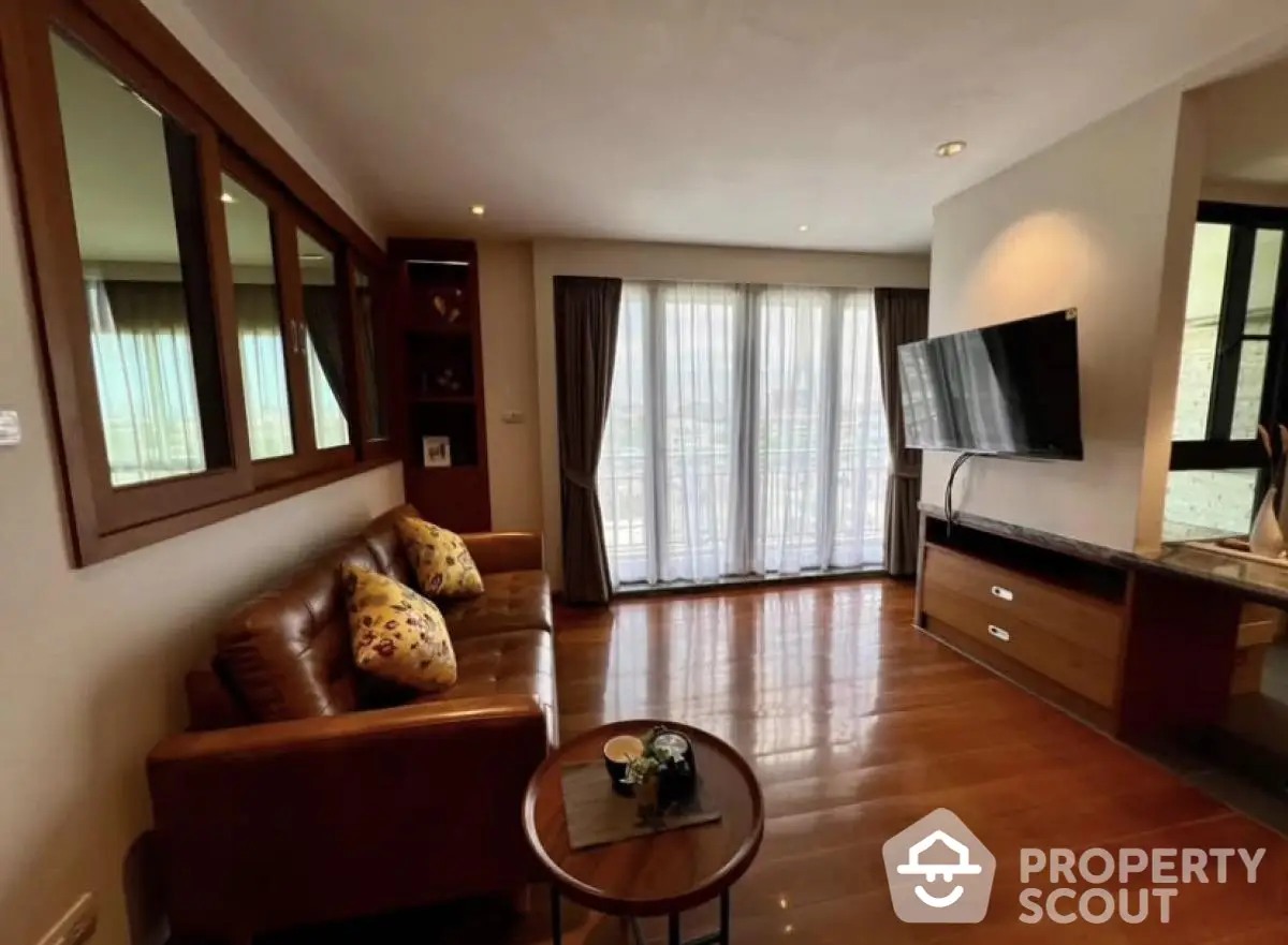 Spacious living room with leather sofa and wall-mounted TV, featuring elegant wooden flooring and large windows.