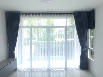 Bright living room with large windows and elegant curtains, offering a serene garden view.