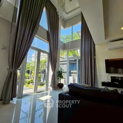 Luxurious living room with high ceilings and large windows offering abundant natural light and garden view.