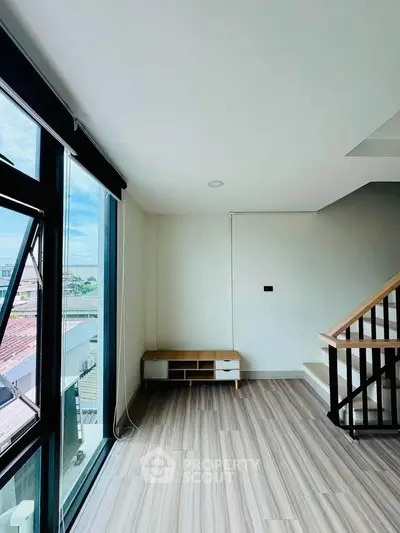 Modern living room with large windows and staircase, featuring sleek flooring and minimalist design.