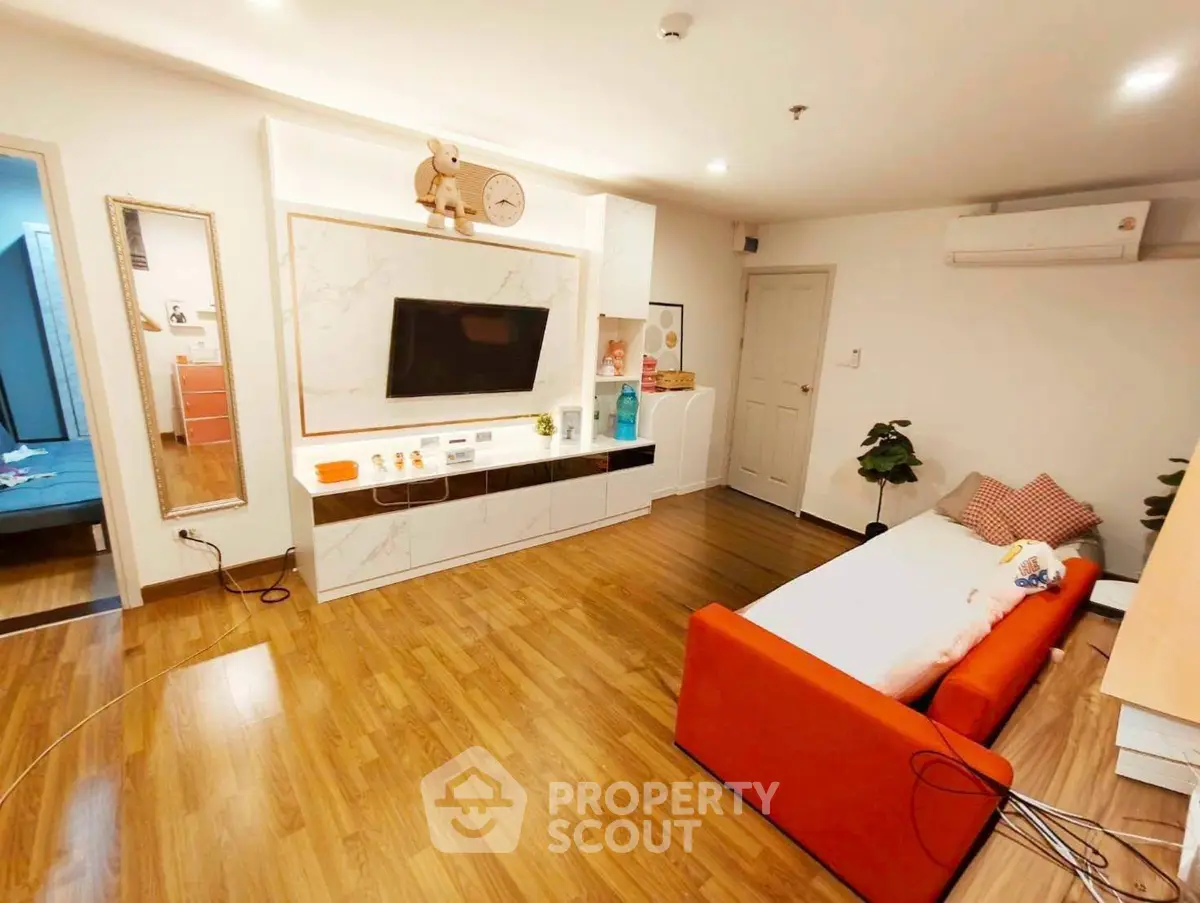 Modern living room with stylish decor and wooden flooring, featuring a cozy orange sofa and wall-mounted TV.