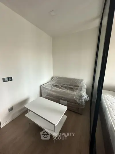 Modern bedroom with minimalist furniture and sleek design, featuring a white table and a bed with protective cover.