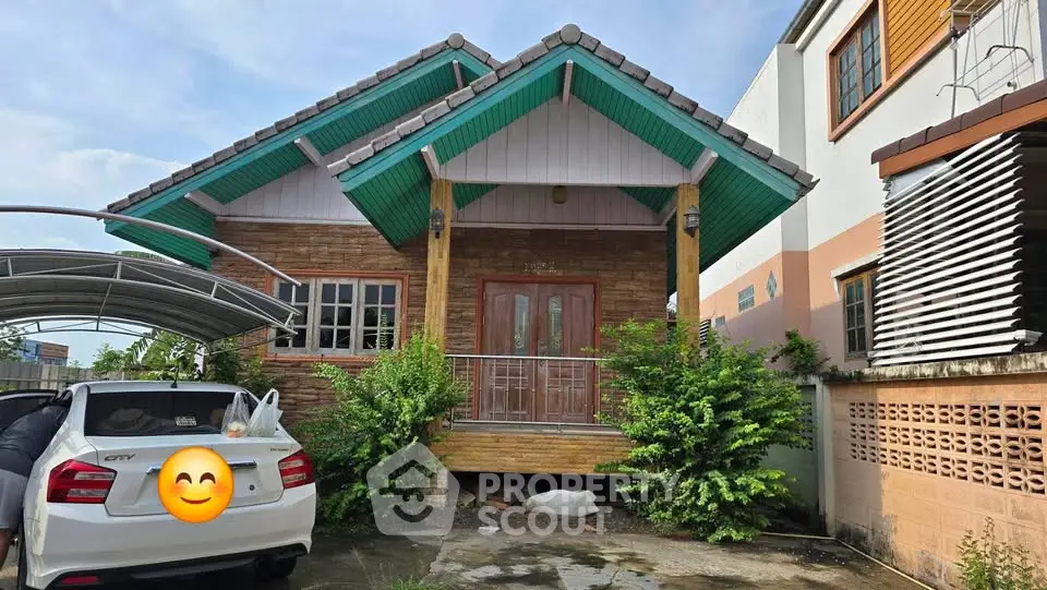 Charming single-story house with green roof and wooden facade, featuring a carport and lush greenery.