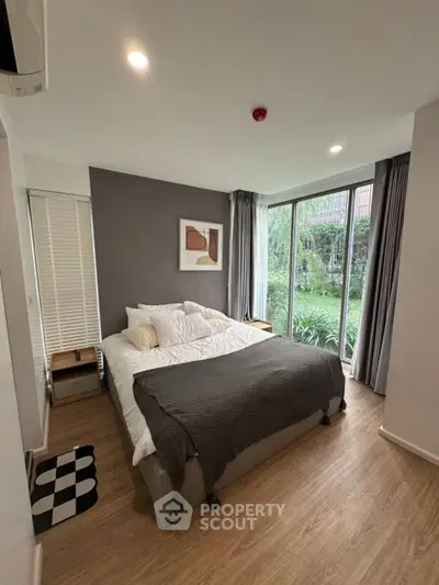 Cozy bedroom with garden view and modern decor, featuring large windows and stylish furnishings.