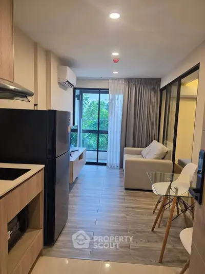 Modern living room with open kitchen, featuring sleek furniture and large windows for natural light.