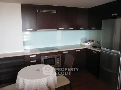 Modern kitchen with dark wood cabinets, glass backsplash, and dining area.