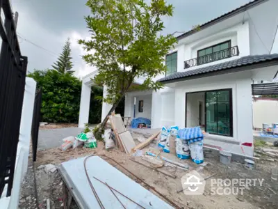 Modern two-story house under construction with white facade and large windows, surrounded by greenery.