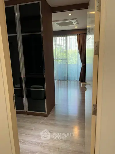 Spacious bedroom with large window and wooden flooring, offering natural light and modern design.
