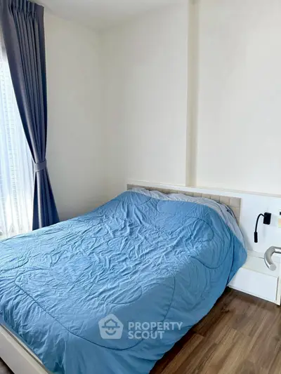 Cozy bedroom with blue bedding and natural light from large window, perfect for relaxation.
