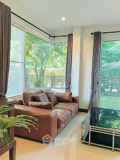Spacious living room with large windows and elegant brown sofa overlooking lush garden.