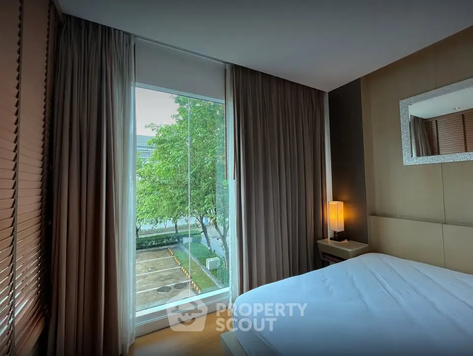 Modern bedroom with large window and garden view, featuring elegant decor and natural light.