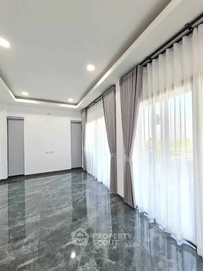 Spacious modern living room with marble flooring and large windows with elegant curtains.